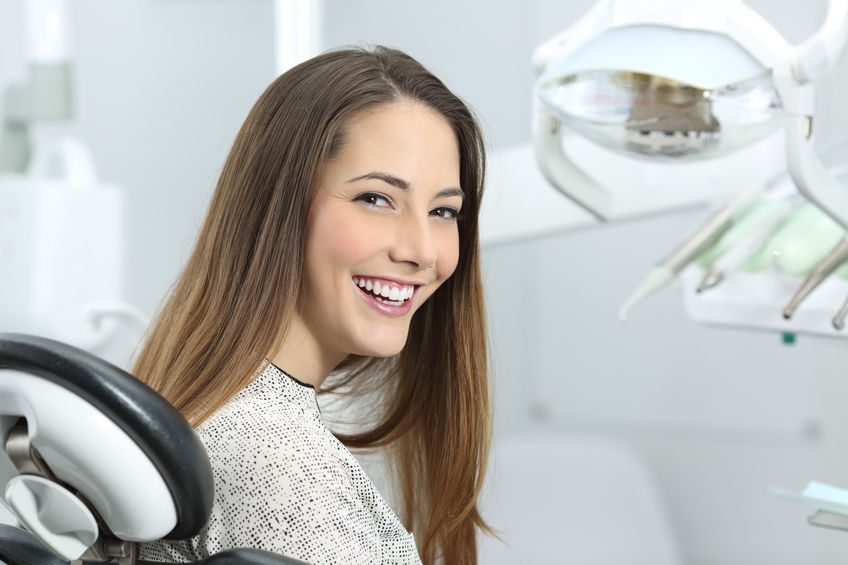 Satisfied dentist patient showing her perfect smile after treatment in a clinic box with medical equipment in the background